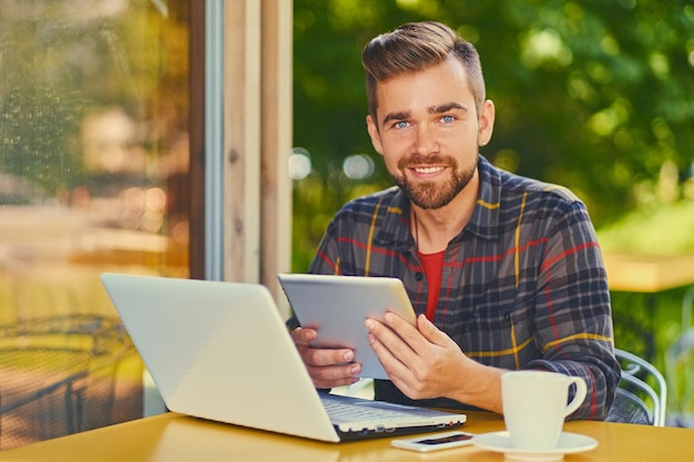 Knappe bebaarde hipster man met laptop in een café.