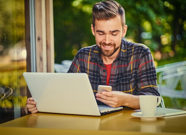 Knappe bebaarde man drinkt koffie tijdens het gebruik van een laptop in een café.