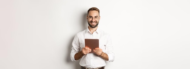 Knappe bebaarde man in glazen met behulp van digitale tablet glimlachend tevreden staande tegen witte backgr