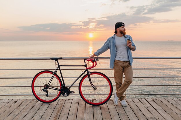 Knappe bebaarde man reizen met de fiets in de ochtend zonsopgang door de zee koffie drinken, gezonde actieve levensstijl reiziger