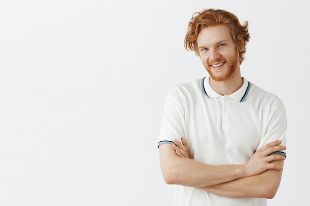 Gratis foto knappe bebaarde roodharige man poseren tegen de witte muur