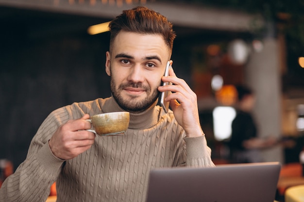 Knappe bedrijfsmens die aan computer en het drinken koffie in een koffie werkt