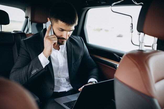 Knappe bedrijfsmens die aan een computer in auto werkt