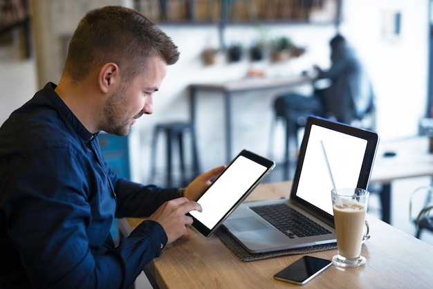 Knappe freelancer met behulp van tablet- en laptopcomputer om zijn bedrijf in café te controleren