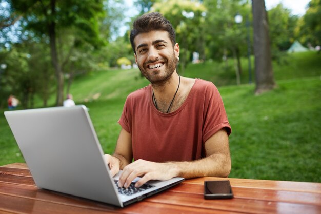 Knappe freelancer werkt op afstand, zit op een bankje met laptop, sluit wifi aan