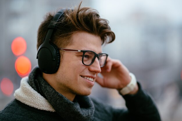 Knappe gelukkig jonge man in brillen, luisteren naar muziek in de koptelefoon
