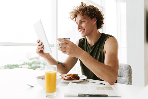 Knappe gelukkige mens gebruikend tabletcomputer en drinkend koffie