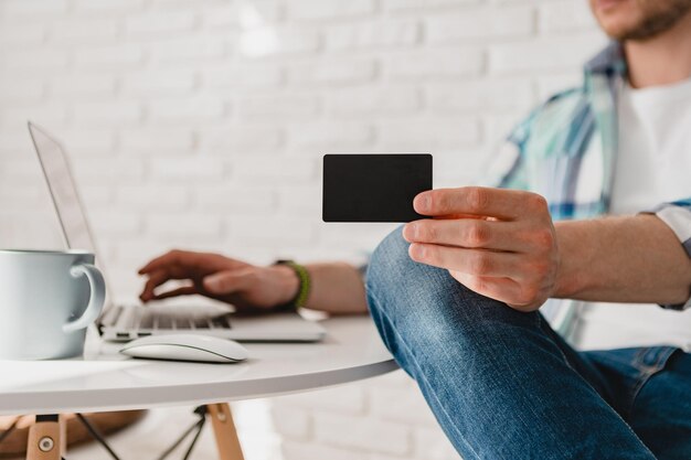 Knappe Glimlachende man in hemd zittend in de keuken thuis aan tafel online werken op laptop