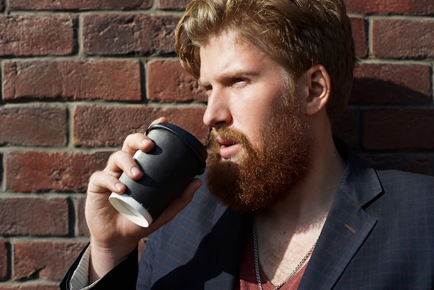 Knappe hipster drinkt koffie buiten met rode bakstenen muur