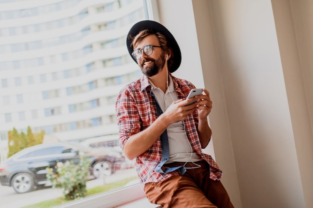 Knappe hipster man met baard in zonnebril SMS-berichten via smartphone en bloggen in sociale netwerken delen van multimedia