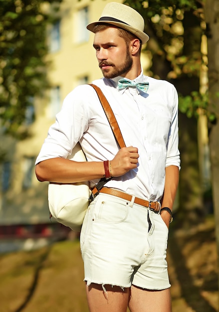 Knappe hipster model man in stijlvolle zomer kleding poseren in hoed met tas