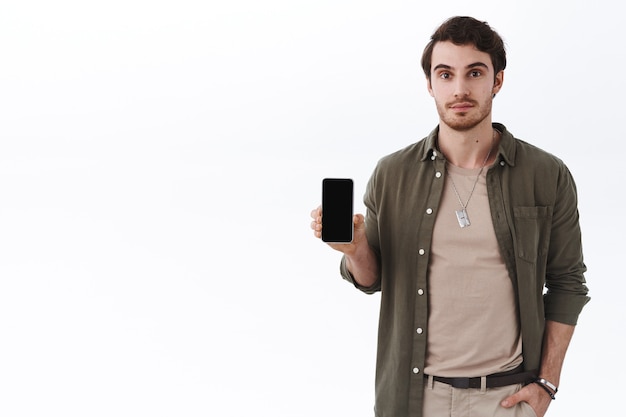 Knappe jonge bebaarde man in stijlvolle outfit, met applicatie, mobiele game of app