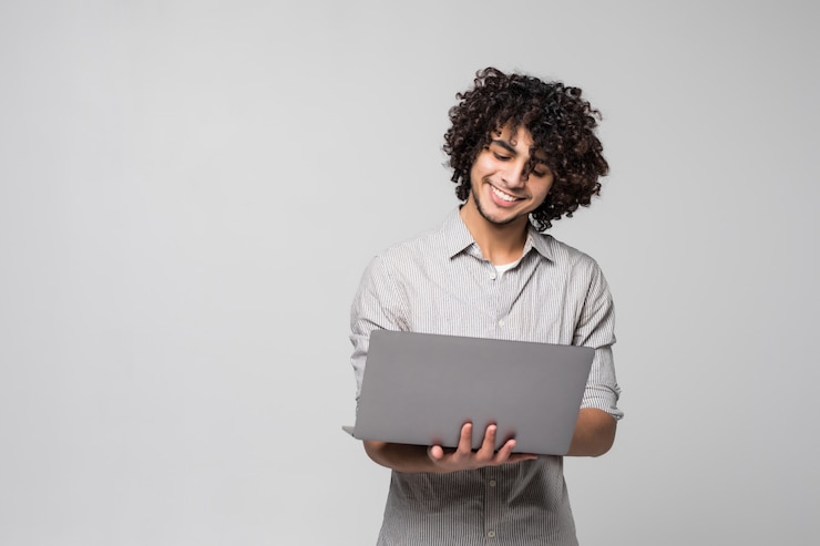 Gratis Foto knappe jonge krullende mens die zich met laptop computer bevindt die op een witte muur wordt geïsoleerd