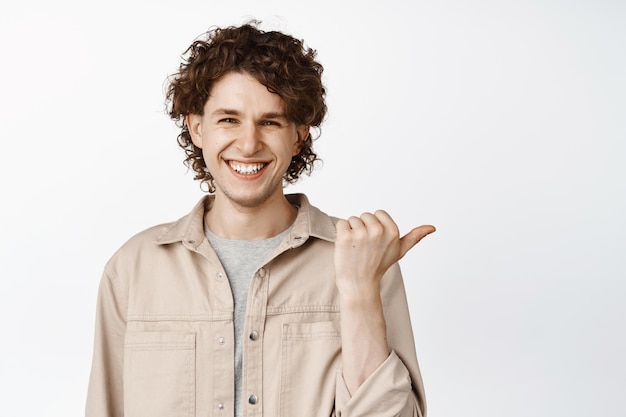 Knappe jonge man die naar rechts wijst glimlachend en reclame witte achtergrond toont