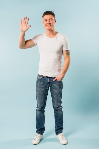 Knappe jonge man haar hand tegen blauwe achtergrond zwaaien