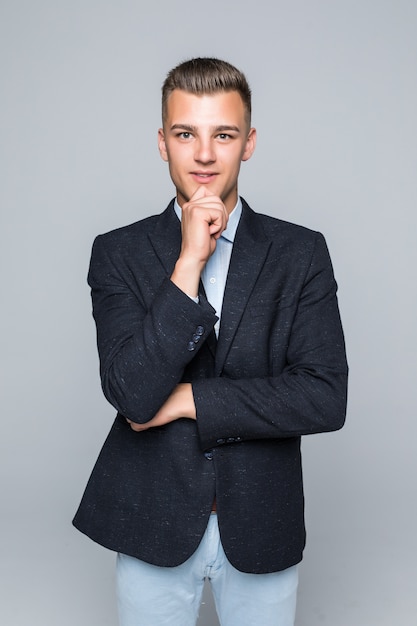 Knappe jonge man in shirt en spijkerbroek houdt zijn arm onder zijn kin op wit wordt geïsoleerd