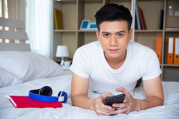 Knappe jonge man liggend op bed en gebruik smartphone