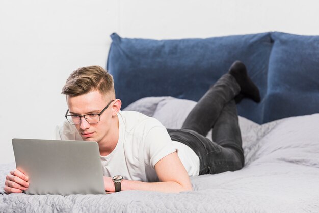 Knappe jonge man liggend op bed met behulp van laptop