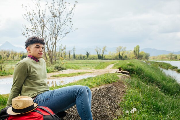 Knappe jonge mannelijke reiziger die op bank van rivier situeert