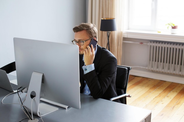 Knappe jonge zakenman in een pak werken met computer op kantoor.