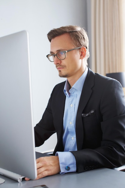 Knappe jonge zakenman in een pak werken met computer op kantoor.