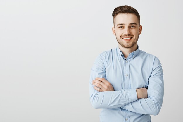 Knappe jonge zakenman met gekruiste armen glimlachend zelfverzekerd