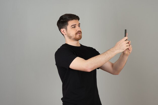 Knappe jongen in zwart t-shirt selfie te nemen op een grijs.