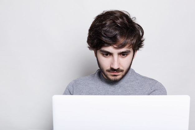 knappe jongen met stijlvol kapsel en trendy baard op zoek met verbazing in het scherm van zijn laptopcomputer