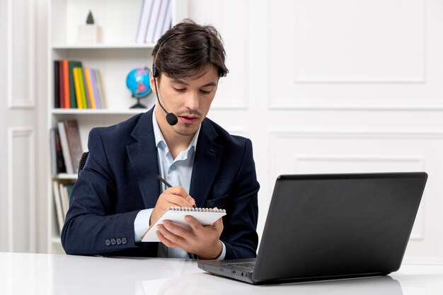 Knappe kerel van de klantenservice met headset en laptop in pak die aantekeningen maakt