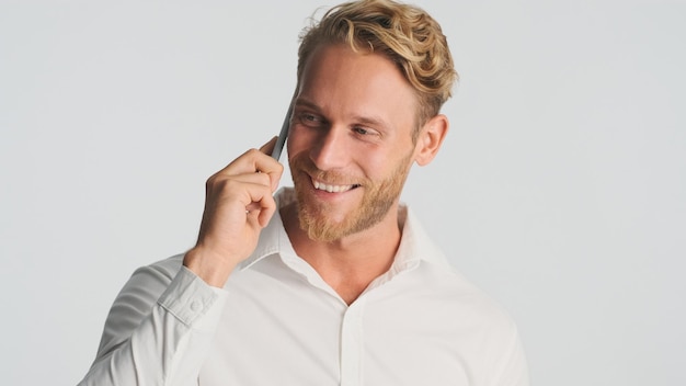 Knappe lachende blonde bebaarde man in shirt bespreken nieuw zakelijk project praten op smartphone geïsoleerd op witte achtergrond moderne technologie