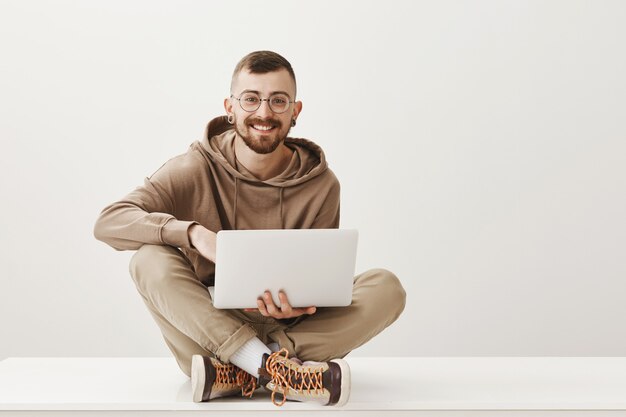 Knappe lachende man zit gekruiste benen en werkt via laptop