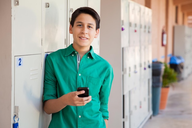 Knappe Latijnse jongen die zijn mobiele telefoon gebruikt in een schoolgang