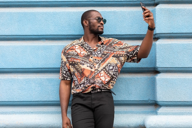 Knappe man die selfie met moderne smartphone buitenshuis neemt