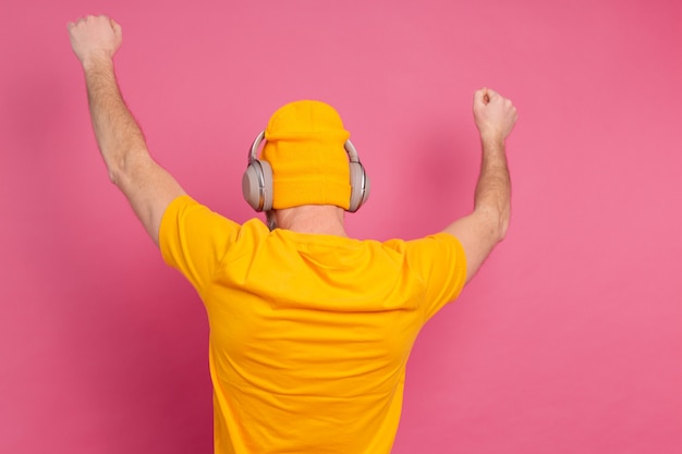 Knappe man in casual dansen met koptelefoon geïsoleerd op roze achtergrond