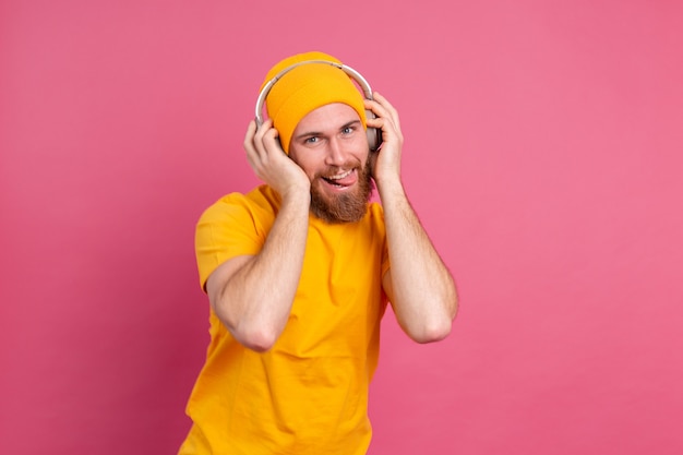 Knappe man in casual dansen met koptelefoon geïsoleerd op roze achtergrond