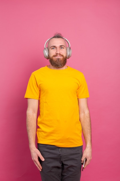 Knappe man in casual luisteren naar muziek met koptelefoon geïsoleerd op roze achtergrond