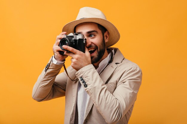 Knappe man in een goed humeur poseren met camera op oranje achtergrond