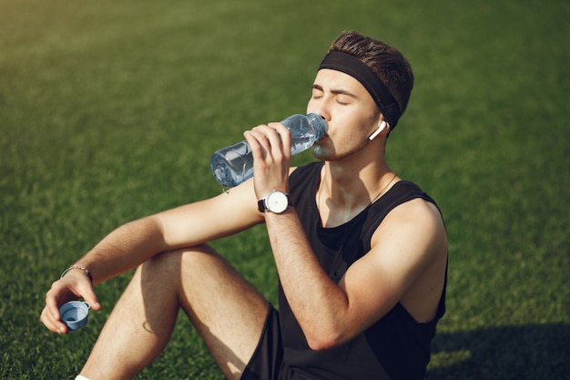 Knappe man in een sport clother drinkwater in een park