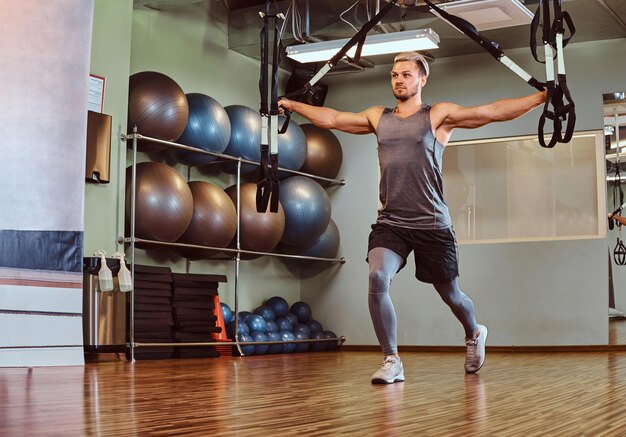 Knappe man in sportkleding trainen met ophangriemen in de fitnessclub.