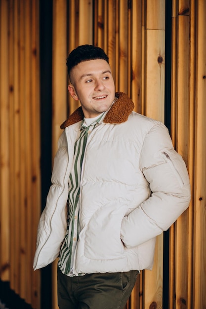 Knappe man in witte winterjas die bij de houten muur staat