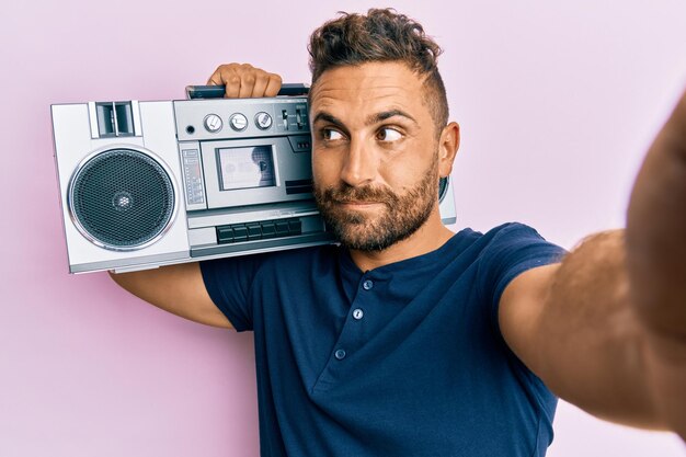 Knappe man met baard die boombox vasthoudt, luisterend naar muziek glimlachend naar de zijkant kijkend en weg starend denkend