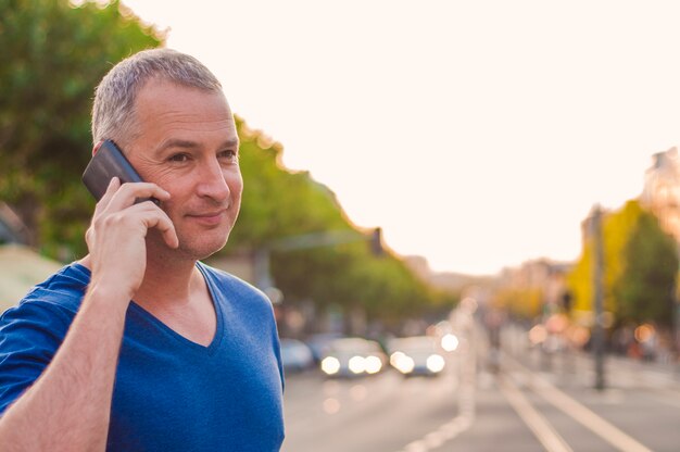 Knappe man met mobiele telefoon, met behulp van smartphone, bellen, praten over de telefoon, permanent op zonnige straat met vervoersverkeer op de achtergrond