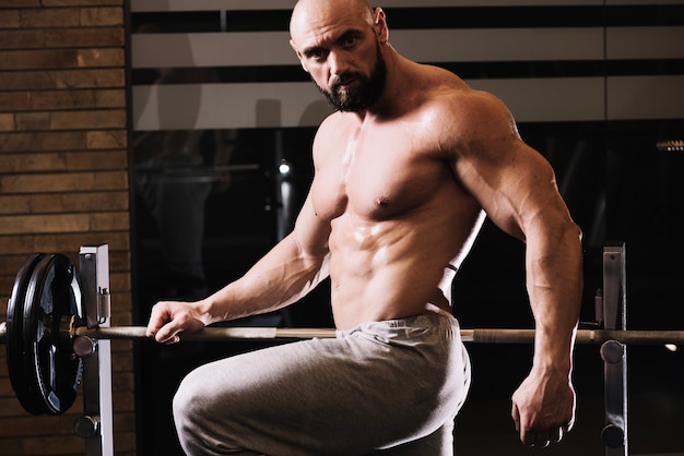 Gratis foto knappe man poseren dichtbij barbell