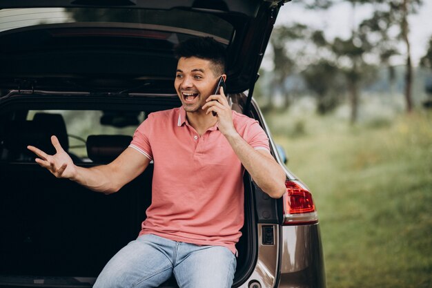 Knappe man praten aan de telefoon bij de auto