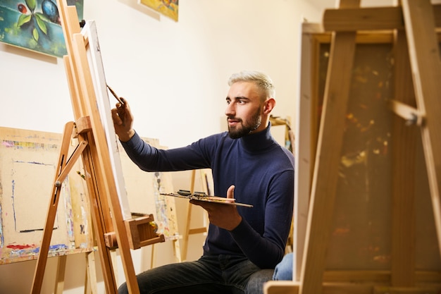 Knappe man tekent een schilderij met oliën en glimlacht