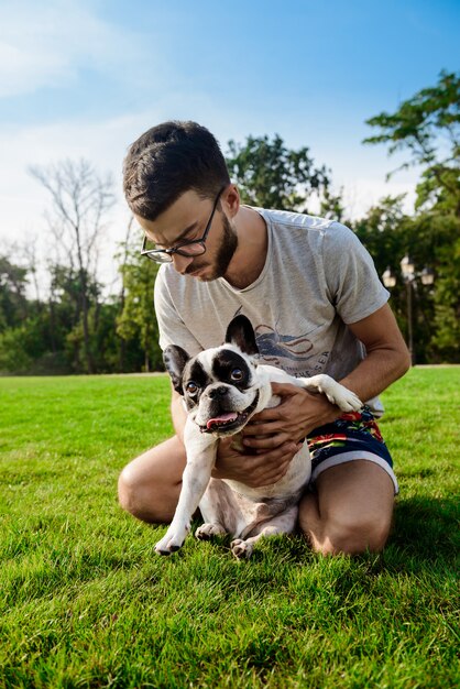 Knappe man zit met Franse bulldog op gras in park