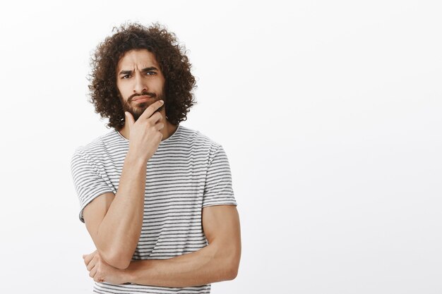 Knappe mannelijke sportman met afro-kapsel, fronsende en aanrakende baard tijdens het nemen van beslissingen, intens en geconcentreerd tijdens kantoorvergaderingen