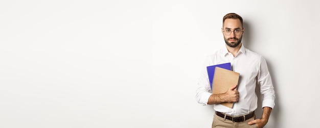Knappe mannelijke werknemer die notitieboekjes vasthoudt en er zelfverzekerd uitziet over een witte achtergrond