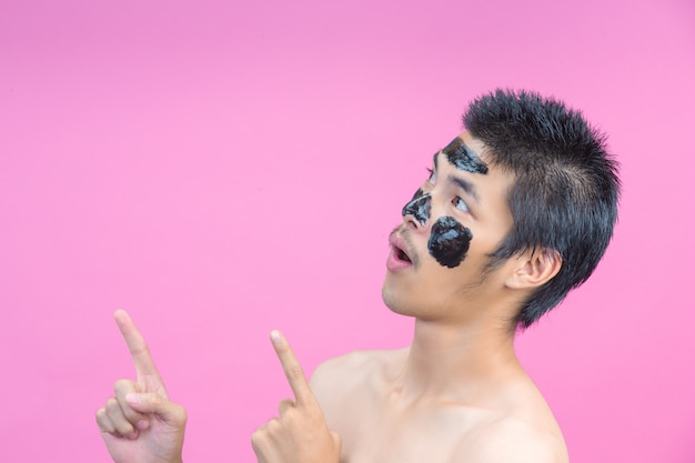 Knappe mannen die zwarte cosmetica op hun gezicht aanbrengen en verschillende houdingen met een roze tonen.