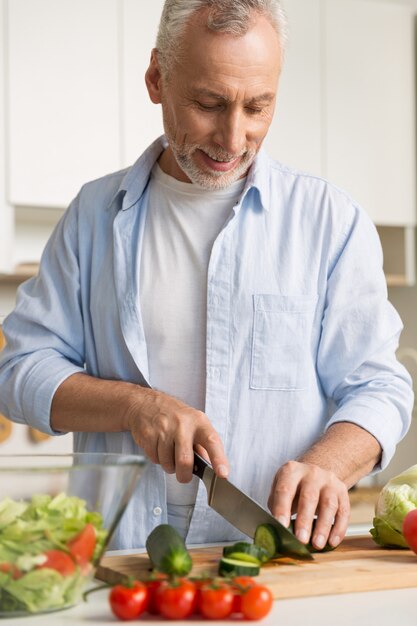 Knappe mens die zich bij de keuken bevindt die laptop en het koken gebruikt